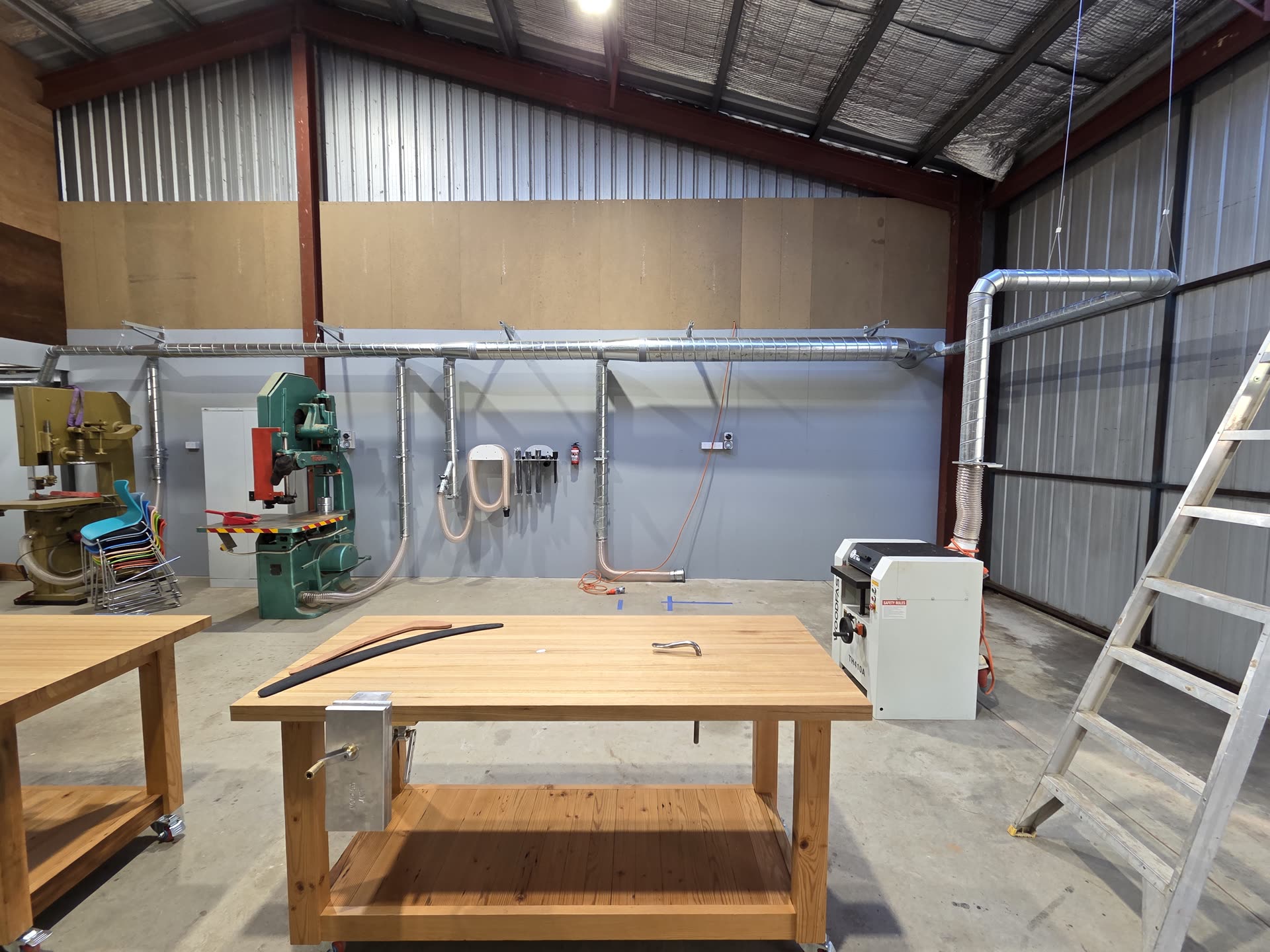 Overhead spiral ducting installed along a woodworking workshop wall, connecting machinery to dust extraction